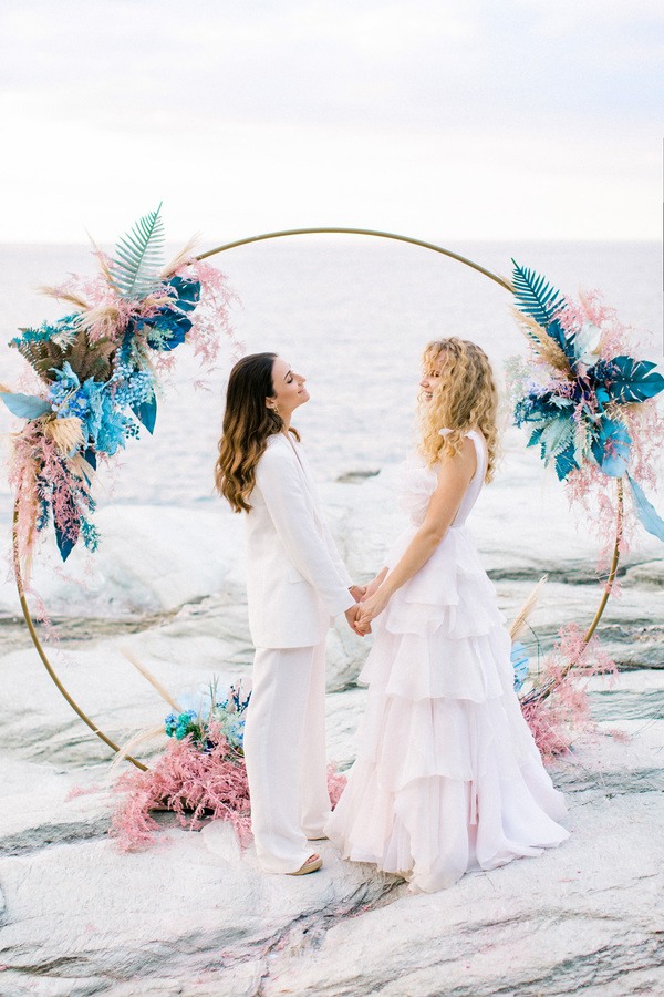 2 brides in front of a flowery arch